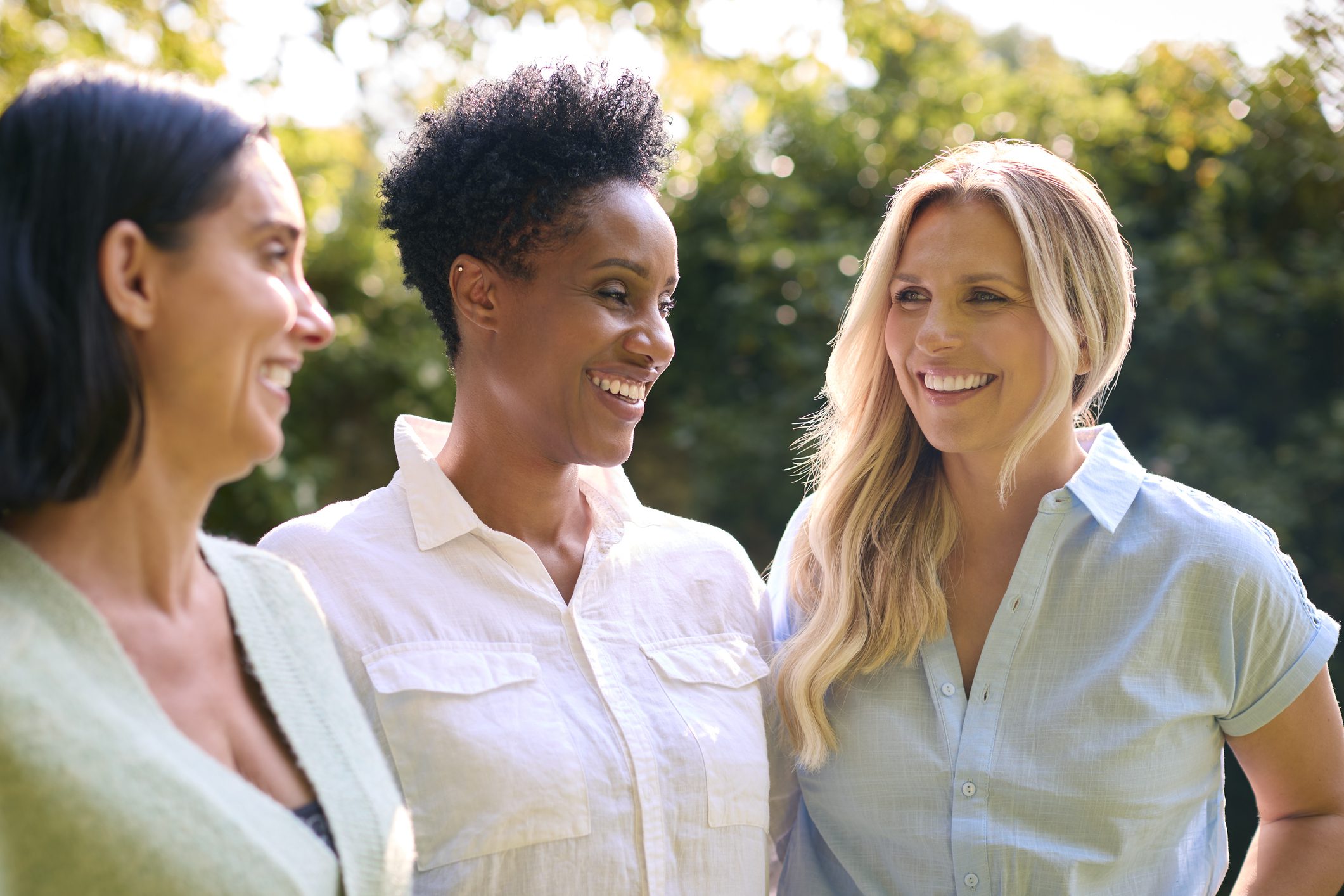 A group of smiling women enjoy each other's presence outdoors.